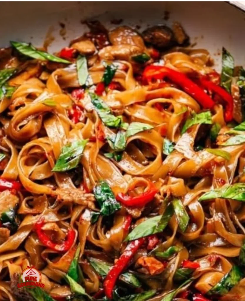 A plate of Thai Drunken Noodles (Pad Kee Mao) garnished with fresh basil and vegetables.