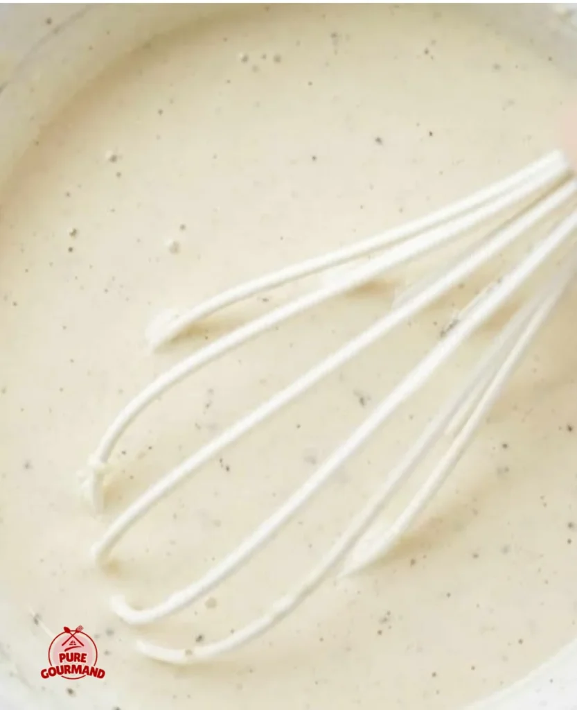 Creamy and tangy Caesar salad dressing in a bowl with fresh ingredients.