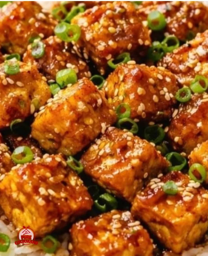 Plate of crispy sticky tofu served with sauce and garnishes.