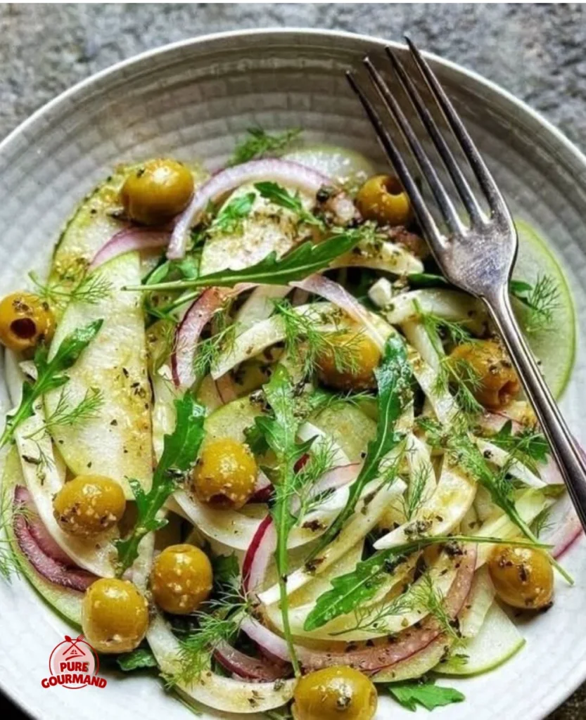Crisp fennel, apple, and arugula salad topped with olives on a rustic plate.